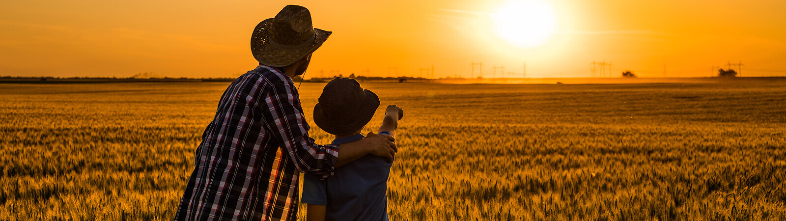 Farmer and farmer's child stand together at sunset